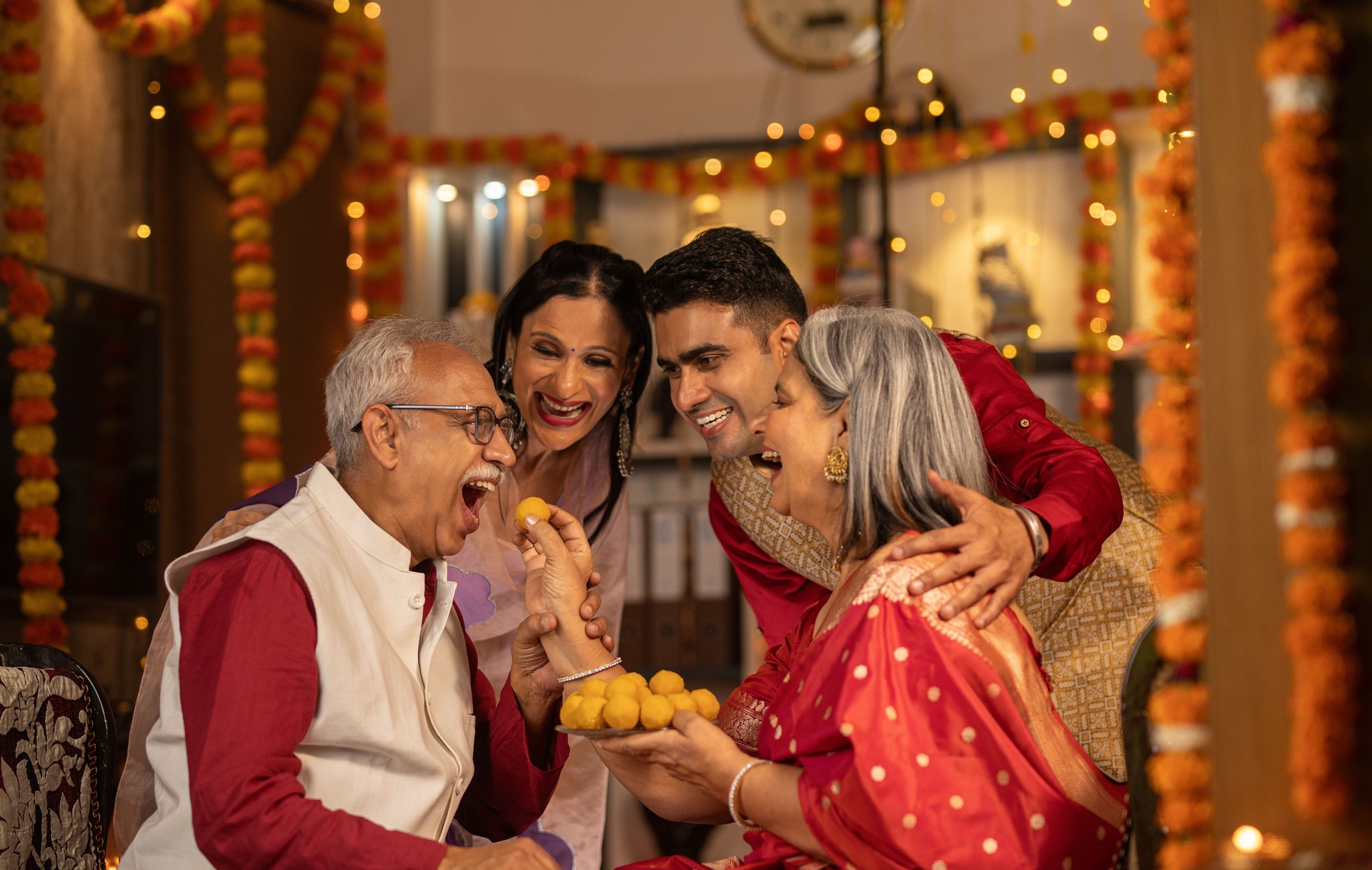 Family looking at senior woman feeding laddoo to husband at home